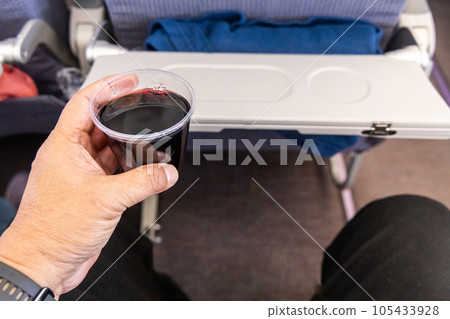 Passenger holding a glass of red wine, served as part of beverage selection during flight in airplane 105433928