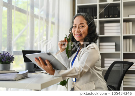 Positive senior businesswoman in elegant suit using digital tablet in personal office 105434346