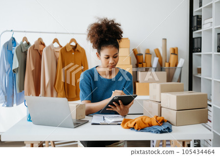 Young African woman running online store Startup small business SME, using smartphone or tablet taking receive and checking online purchase shopping order in office 105434464