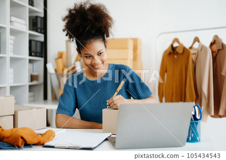 Young African woman running online store Startup small business SME, using smartphone or tablet taking receive and checking online purchase shopping order in office 105434543