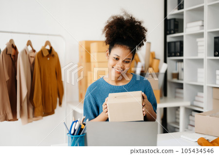Young African business owner woman prepare parcel box and standing check online orders for deliver to customer on tablet, laptop Shopping Online concept. in office 105434546