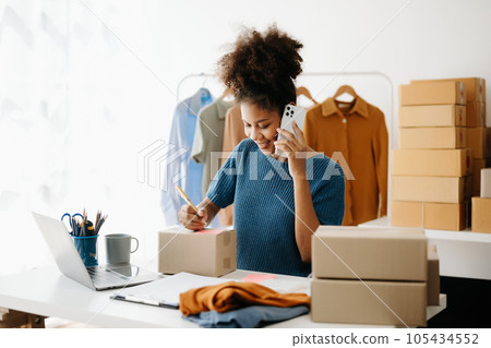 Young African business owner woman prepare parcel box and standing check online orders for deliver to customer on tablet, laptop Shopping Online concept. in office 105434552