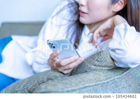 A woman lying on the sofa and using a smartphone [parts cut] 105434681