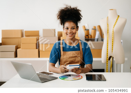 Startup small business SME, Entrepreneur owner African woman using smartphone or tablet taking receive and checking online purchase shopping order to preparing pack product box. in office. Startup small business SME, Entrepreneur owner African woman using smartphone or tablet taking receive and checking online purchase shopping order to preparing pack product box. in office. 105434991