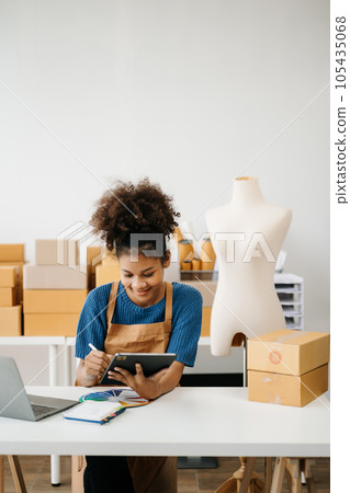 Startup small business SME, Entrepreneur owner African woman using smartphone or tablet taking receive and checking online purchase shopping order to preparing pack product box. in office. Startup small business SME, Entrepreneur owner African woman using smartphone or tablet taking receive and checking online purchase shopping order to preparing pack product box. in office. 105435068