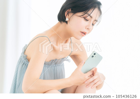 Young woman operating a smartphone while doing skin care 105436126