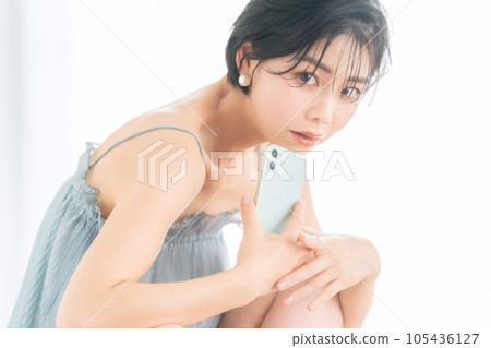 Young woman operating a smartphone while doing skin care 105436127