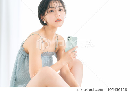 Young woman operating a smartphone while doing skin care 105436128