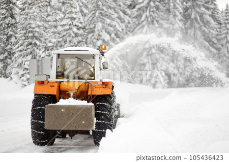 A snowplow truck clearing a snow-covered road in the European Alps while a snowstorm. Drifts and snow drifts during a snowfall. A snowplow truck clearing a snow-covered road in the European Alps while a snowstorm. Drifts and snow drifts during a snowfall. 105436423