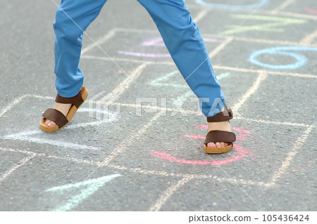 Little boy's legs and hopscotch drawn on asphalt. Child playing hopscotch game on playground on spring day. 105436424