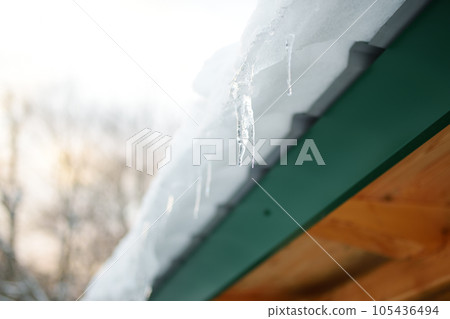 The roof of a house on a snowy winter day among thaw. Cleaning the roofing from snow and icicles. 105436494