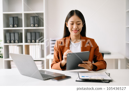 Successful Asian Businesswoman Analyzing Finance on Tablet and Laptop at Office Desk tax, report, accounting, statistics, and analytical research concept. Successful Asian Businesswoman Analyzing Finance on Tablet and Laptop at Office Desk tax, report, accounting, statistics, and analytical research concept. 105436527