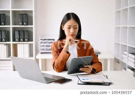 Successful Asian Businesswoman Analyzing Finance on Tablet and Laptop at Office Desk tax, report, accounting, statistics, and analytical research concept. Successful Asian Businesswoman Analyzing Finance on Tablet and Laptop at Office Desk tax, report, accounting, statistics, and analytical research concept. 105436557