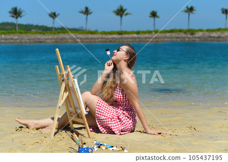 Young artist woman sitting at the beach with a jar with paint brushes and easel close to sea and palms in summer Young artist woman sitting at the beach with a jar with paint brushes and easel close to sea and palms in summer 105437195