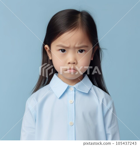 Portrait of a little serious Asian girl with straight black hair. Closeup face of an unhappy Chinese child on a blue background. Japanese kid with no expression in a blue shirt looking at camera. 105437243