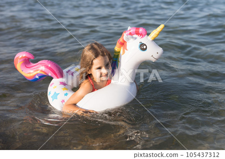 Happy baby girl swimming on an inflatable swimming unicorn in the sea Happy baby girl swimming on an inflatable swimming unicorn in the sea 105437312