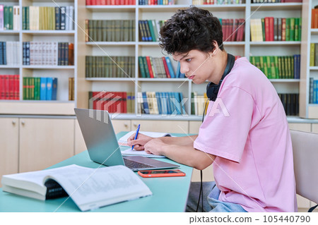 Young male student sitting with laptop with books in college library Young male student sitting with laptop with books in college library 105440790