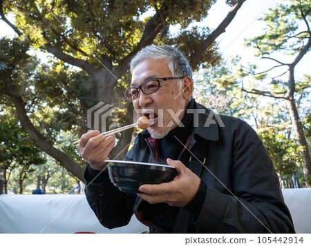 An older asian man eating noodles and soup with chopsticks 105442914