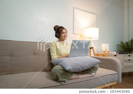 young woman in headphones using laptop listening to music relax sitting on the sofa at home 105443040