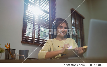 Asia women wear wireless headphone study online write notes look at laptop in living room, distant education 105443079
