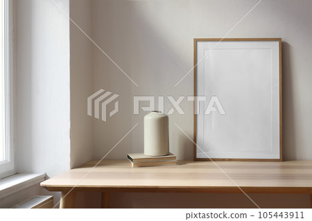 Stylish moody interior. Living room with ceramic vase, old books on wooden table near window. . Blank wooden picture frame, poster mockup. Minimalist concept of home decor. Scandinavian design. Stylish moody interior. Living room with ceramic vase, old books on wooden table near window. . Blank wooden picture frame, poster mockup. Minimalist concept of home decor. Scandinavian design. 105443911