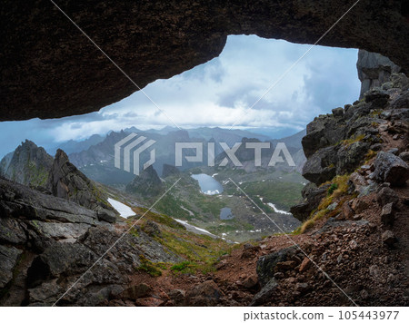 Mysterious, mystical and unusual caves and landscapes of the Sayan mountains. View of the great mountain through the cave. Mountain lakes is far away in the valley. Mysterious, mystical and unusual caves and landscapes of the Sayan mountains. View of the great mountain through the cave. Mountain lakes is far away in the valley. 105443977