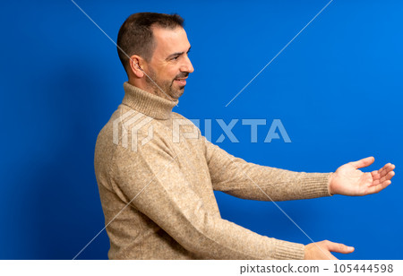 Free hugs, come into my arms. Side view of happy bearded man in his 40s stretching hands and smiling broadly, embracing, sharing love. Indoor studio shot isolated on blue background. Free hugs, come into my arms. Side view of happy bearded man in his 40s stretching hands and smiling broadly, embracing, sharing love. Indoor studio shot isolated on blue background. 105444598