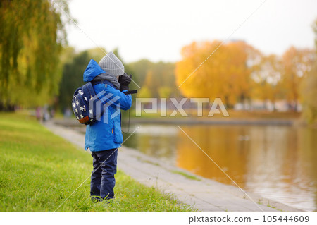 Little boy having fun during stroll in city park at sunny autumn day. Child exploring nature with binoculars. Little boy having fun during stroll in city park at sunny autumn day. Child exploring nature with binoculars. 105444609