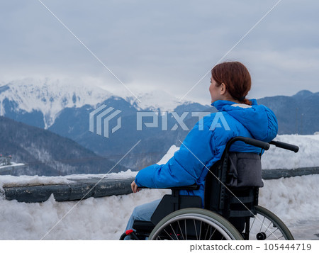 Rear view of a woman in a wheelchair travels in the mountains in winter. Rear view of a woman in a wheelchair travels in the mountains in winter. 105444719
