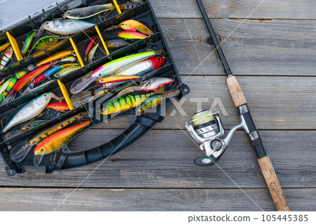 A fishing tackle box, complete with lures and fishing gear on a wooden background on top. A set of fishing lures for spinning fishing 105445385
