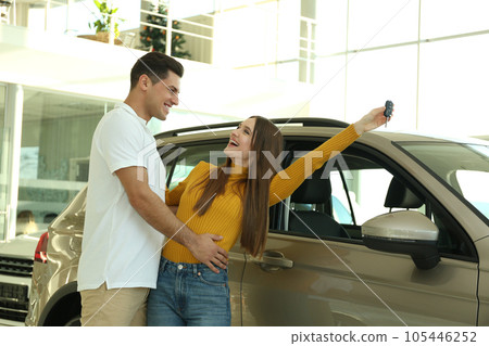 Happy couple with car key in modern auto dealership 105446252