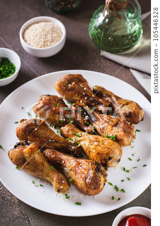 Appetizing baked chicken legs with chives and sesame seeds on a plate vertical view Appetizing baked chicken legs with chives and sesame seeds on a plate vertical view 105446328