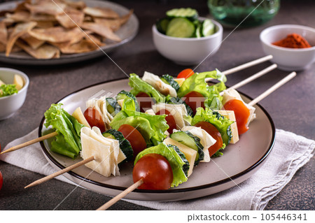 Snack on skewers of tomatoes, cucumber, cheese, pita bread and lettuce on a plate Snack on skewers of tomatoes, cucumber, cheese, pita bread and lettuce on a plate 105446341