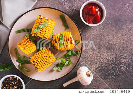 Baked sweet corn cobs with butter, garlic and herbs on a plate top view Baked sweet corn cobs with butter, garlic and herbs on a plate top view 105446419