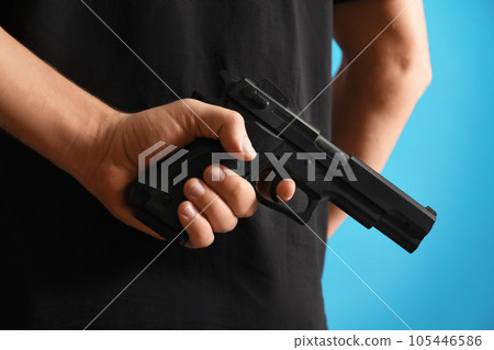 Man holding gun on blue background, closeup 105446586