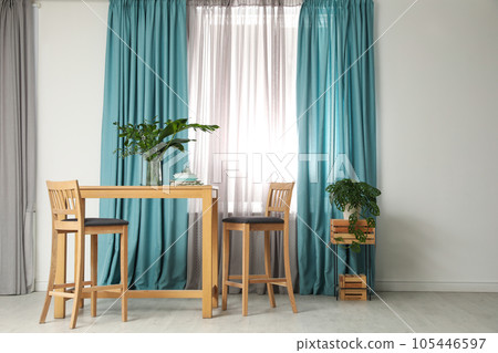 Stylish wooden table and chairs near window with elegant curtains in room Stylish wooden table and chairs near window with elegant curtains in room 105446597