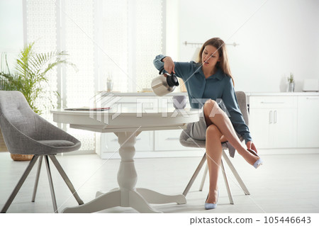 Young woman pouring coffee into cup while putting on shoes at home in morning 105446643