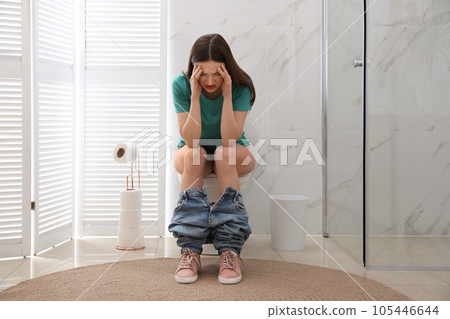 Woman suffering from hemorrhoid on toilet bowl in rest room 105446644