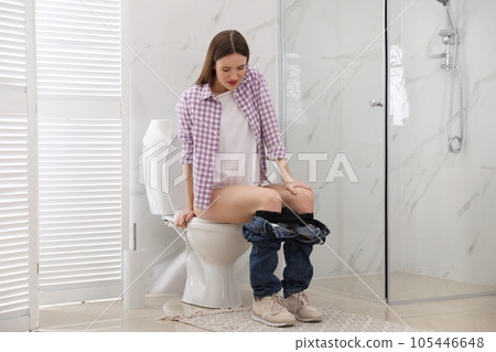 Woman suffering from hemorrhoid on toilet bowl in rest room 105446648
