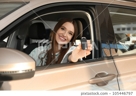 Beautiful woman with car key sitting in modern auto at dealership 105446797