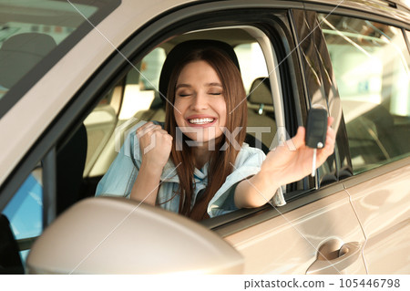 Beautiful woman with car key sitting in modern auto at dealership 105446798
