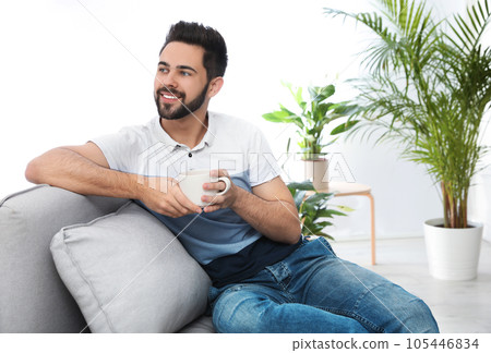 Young man with cup of drink relaxing on couch at home 105446834