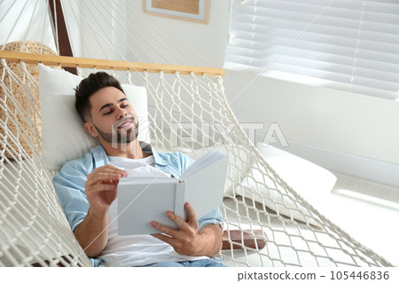 Young man reading book in hammock at home 105446836
