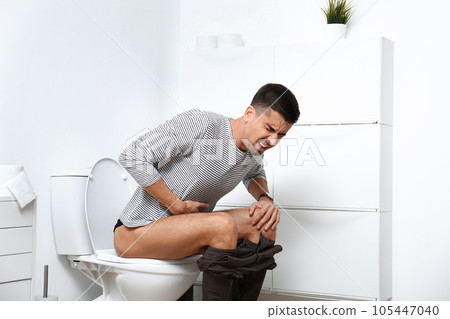 Man with stomach ache sitting on toilet bowl in bathroom 105447040