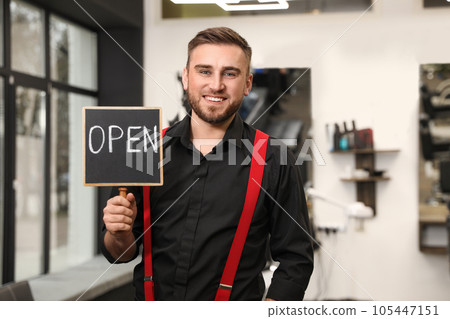 Young business owner holding OPEN sign in his barber shop 105447151