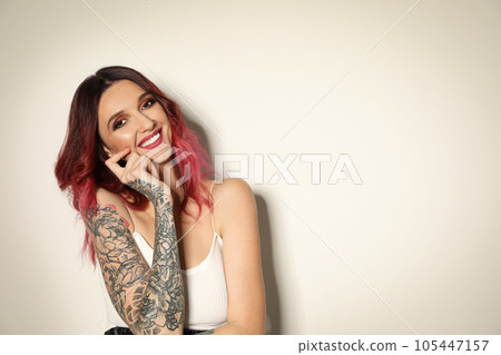 Beautiful woman with tattoos on arms against light background. Space for text 105447157