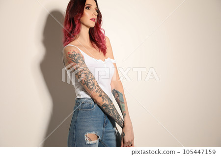 Beautiful woman with tattoos on arms against light background 105447159
