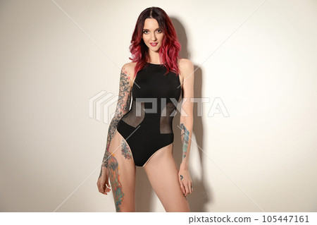 Beautiful woman with tattoos on body against light background 105447161