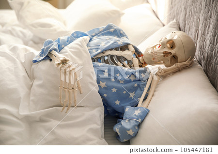 Human skeleton in pajamas lying on bed indoors 105447181