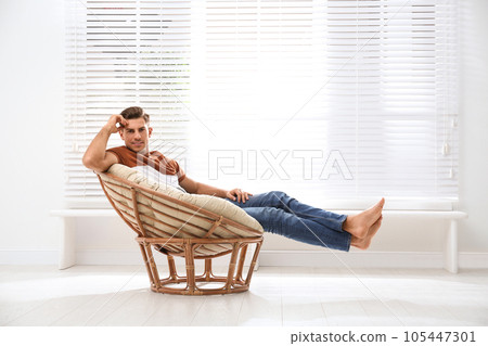 Attractive man relaxing in papasan chair near window at home 105447301
